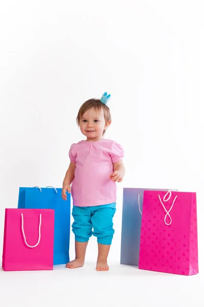 Kleines Mädchen steht mit bunten Papiertüten isoliert auf weißem Hintergrund. — Stockfoto