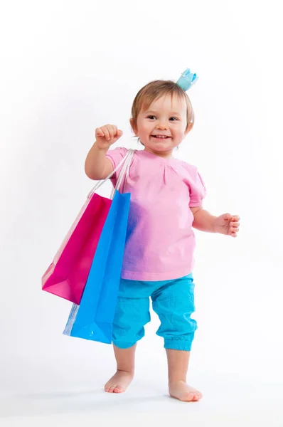 Lief meisje in roze en blauw design met papieren zakken geïsoleerd op witte achtergrond. — Stockfoto