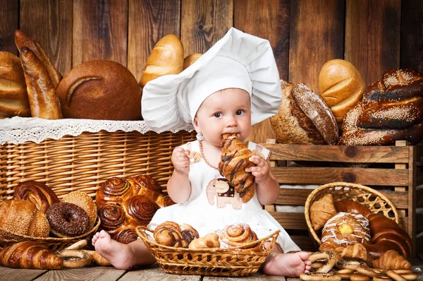 Criança pequena cozinha um croissant no fundo de cestas com rolos e pão . — Fotografia de Stock