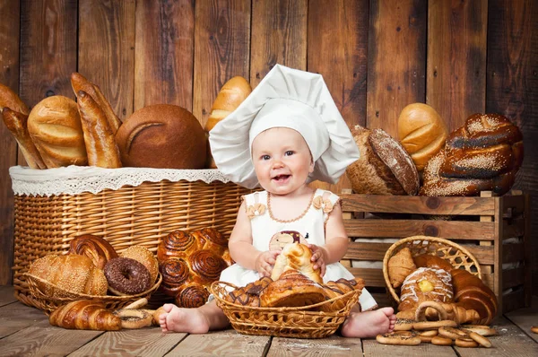 Malé dítě vaří croissant v pozadí košů s rohlíky a chleba. — Stock fotografie