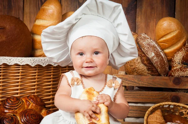 Klein kind kookt een croissant in de achtergrond van manden met broodjes en brood. — Stockfoto