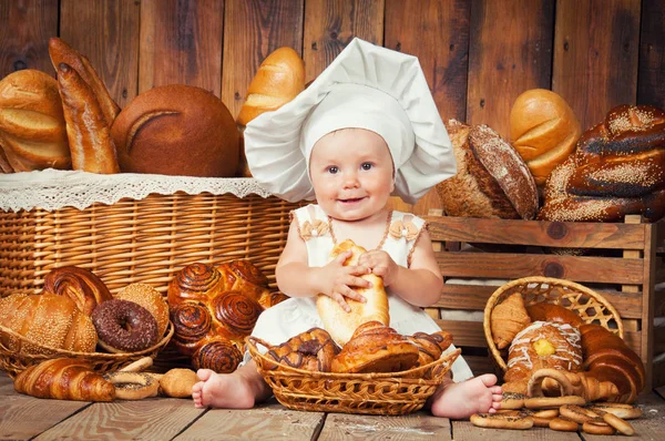 Criança pequena cozinha um croissant no fundo de cestas com rolos e pão . — Fotografia de Stock