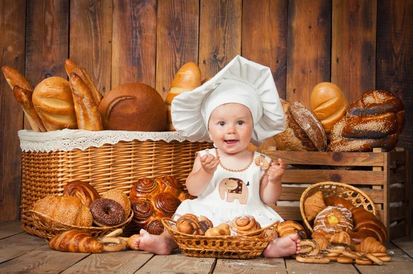 Criança pequena cozinha um croissant no fundo de cestas com rolos e pão . — Fotografia de Stock