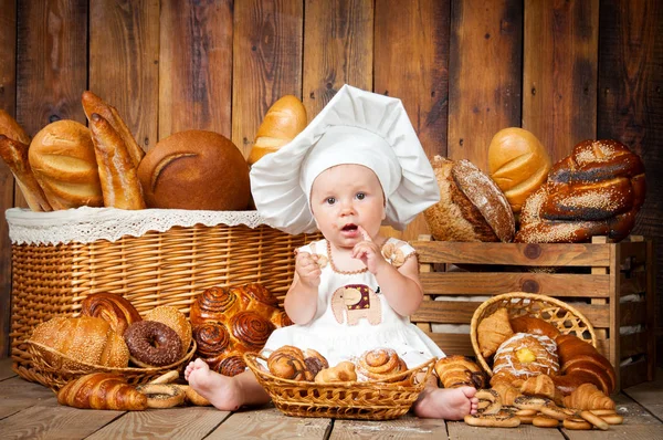 Malé dítě vaří croissant v pozadí košů s rohlíky a chleba. — Stock fotografie