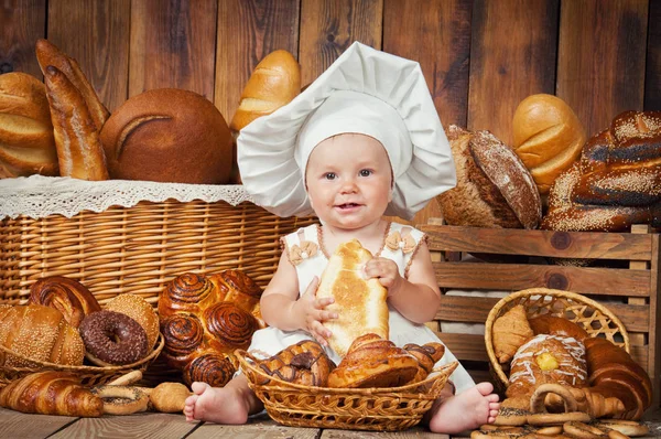 Malé dítě vaří croissant v pozadí košů s rohlíky a chleba. — Stock fotografie