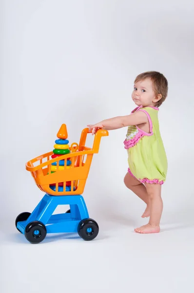 Menina com carrinho de compras de brinquedo. Isolado sobre fundo branco . — Fotografia de Stock