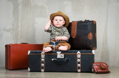 Bir bavul ve onun elinde bir fotoğraf makinesi ile çocuk oturur