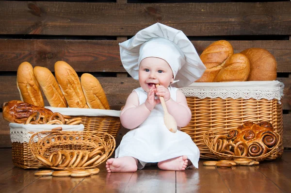 Kind kookt een croissant in de achtergrond van manden met broodjes en brood. — Stockfoto