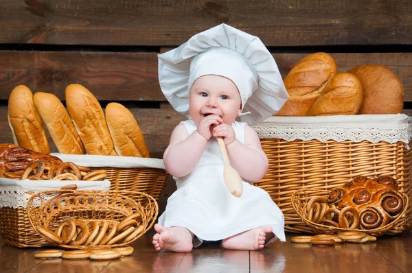 Porträt Kind kocht im Hintergrund Körbe mit Brötchen und Brot. — Stockfoto