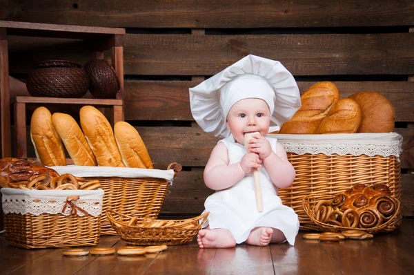 Kind kookt eten die een bagel op de achtergrond van manden met broodjes en brood. — Stockfoto