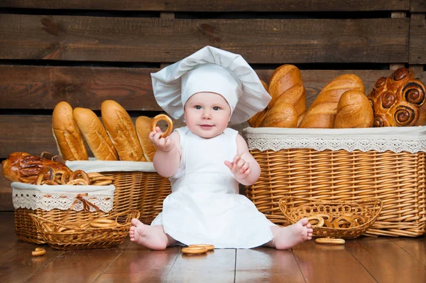 Kinderköche essen einen Bagel auf dem Hintergrund von Körben mit Brötchen und Brot. — Stockfoto