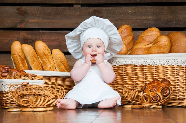 Kinderköche essen einen Bagel auf dem Hintergrund von Körben mit Brötchen und Brot. — Stockfoto