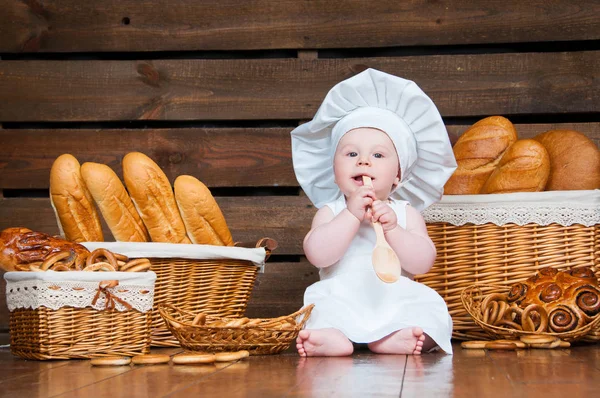 Kind kookt eten die een bagel op de achtergrond van manden met broodjes en brood. — Stockfoto