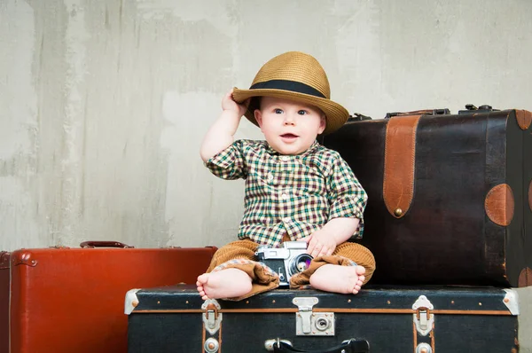 Bir bavul ve onun elinde bir fotoğraf makinesi ile çocuk oturur
