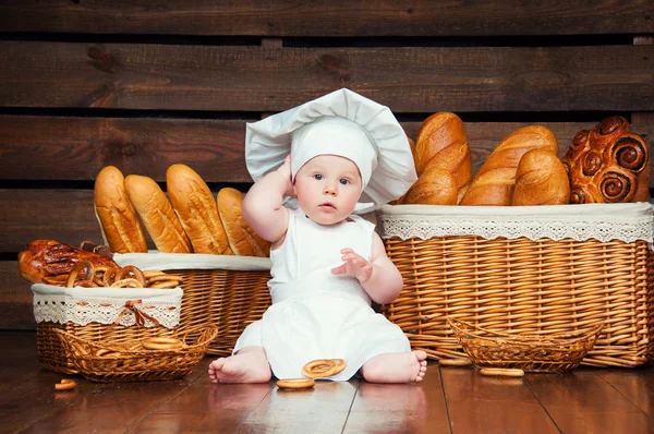 Kind kookt eten die een bagel op de achtergrond van manden met broodjes en brood. — Stockfoto