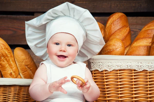 Kind kookt eten die een bagel op de achtergrond van manden met broodjes en brood. — Stockfoto