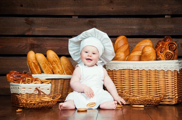 Criança cozinha comer um bagel no fundo de cestas com rolos e pão . — Fotografia de Stock