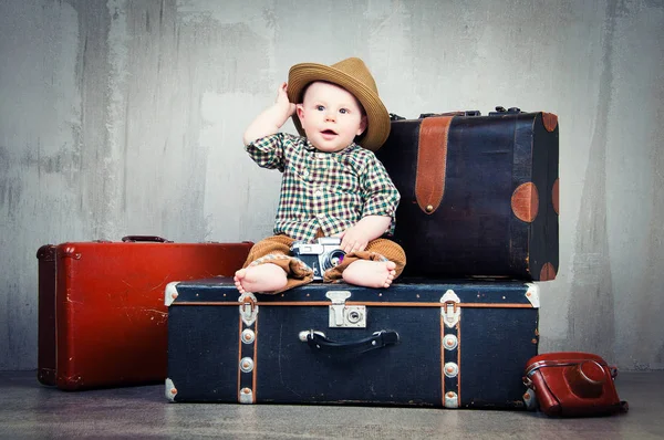 Bir bavul ve onun elinde bir fotoğraf makinesi ile çocuk oturur