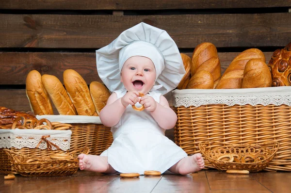 Kinderköche essen einen Bagel auf dem Hintergrund von Körben mit Brötchen und Brot. — Stockfoto