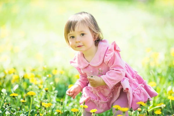 Menina em vestido rosa com dente de leão na grama verde . — Fotografia de Stock