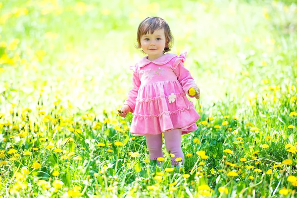Девушка в розовом платье с одуванчиком на зеленой траве . — стоковое фото