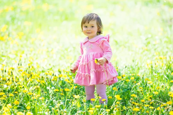 Yeşil çimenlerin üzerinde karahindiba ile pembe elbiseli kız. — Stok fotoğraf