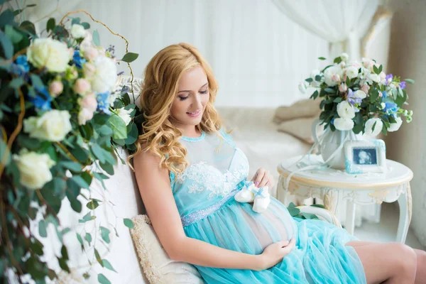 Het meest charmante zwanger meisje in een zachte interieur met verse bloemen. — Stockfoto