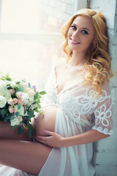 Piękna dziewczyna w ciąży, uśmiechając się, siedząc na okna z bukietem kwiatów. — Zdjęcie stockowe