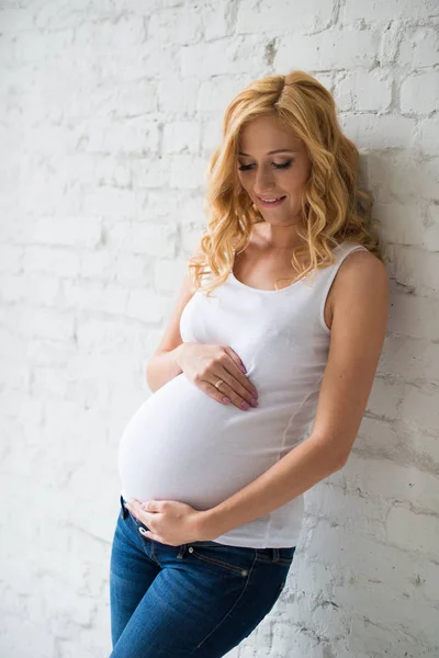 Uma menina grávida doce está de pé e abraçando sua barriga . — Fotografia de Stock