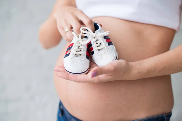 Έγκυος κορίτσι με πάνινα παπούτσια μωρών για το φόντο της κοιλιάς. — Φωτογραφία Αρχείου