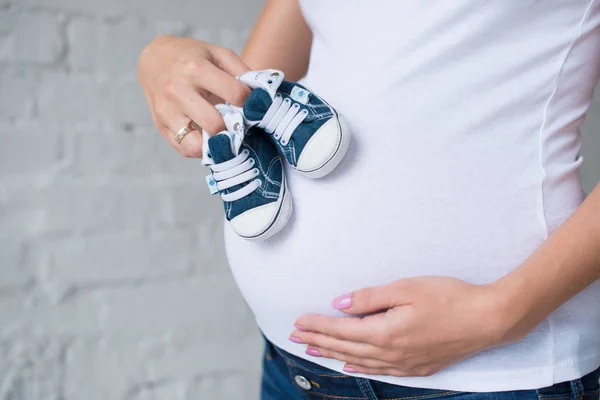 Karın arka plan üzerinde bebek spor ayakkabı ile hamile kız. — Stok fotoğraf