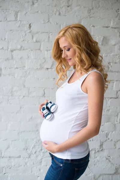 Beautiful red-haired pregnant girl with baby sneakers. — Stock Photo, Image