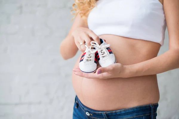 Karın arka plan üzerinde bebek spor ayakkabı ile hamile kız. — Stok fotoğraf