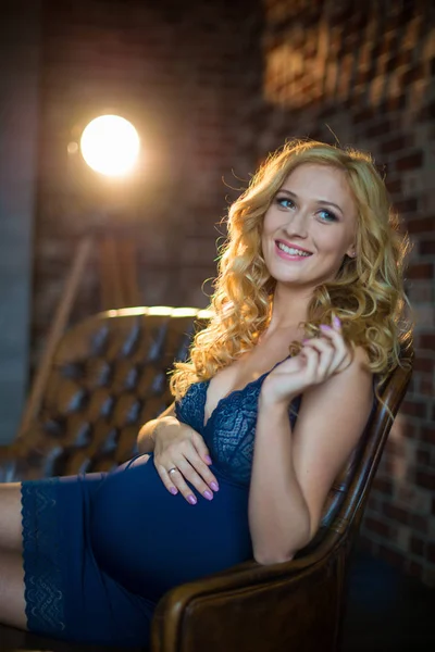 A beautiful pregnant girl is sitting on the couch in a loft interior. — Stock Photo, Image