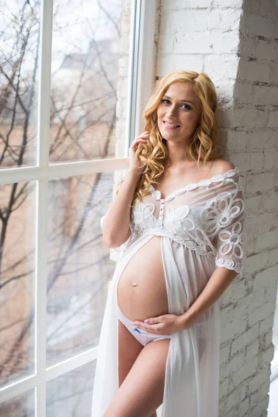 Очаровательная беременная девушка смотрит в окно . — стоковое фото