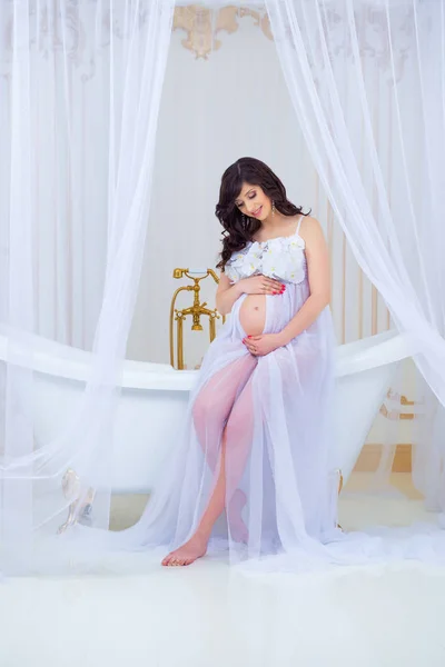 Нежная беременность. Красивая беременная в белом платье с орхидеями — стоковое фото