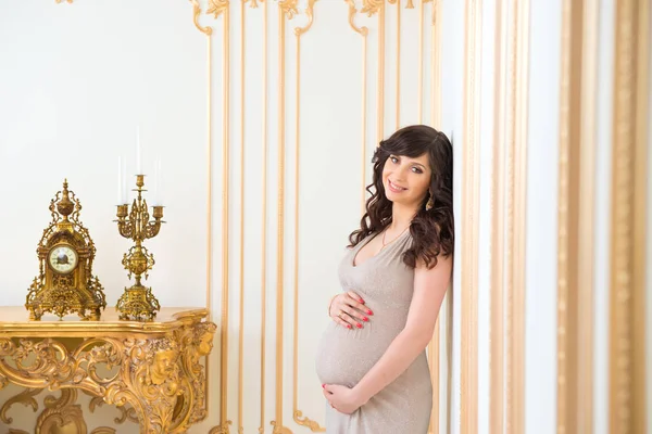 ファッショナブルな妊娠中のお母さんのおなかを抱き締める黄金のドレス — ストック写真