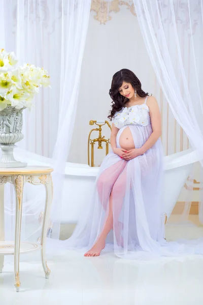 Embarazo suave. Hermosa embarazada en vestido blanco claro con orquídeas — Foto de Stock