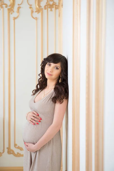 Fashionabla gravid mamma i gyllene klänning kramas mage — Stockfoto