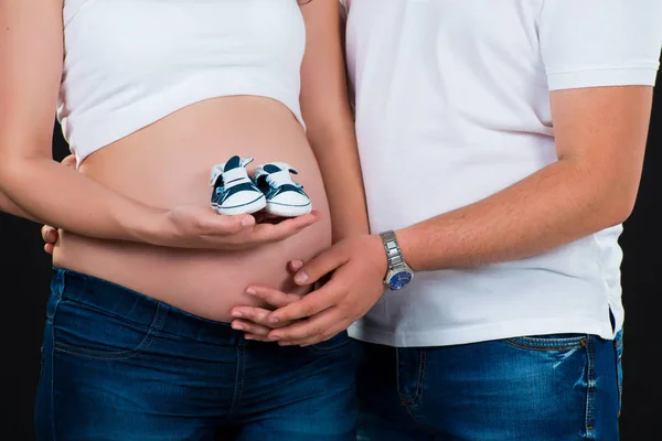 Gravid flicka håller barnens kediks i händerna på magen — Stockfoto