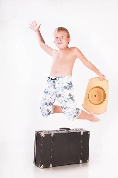 Malý chlapec cestovatel v klobouku sedí na kufru — Stock fotografie