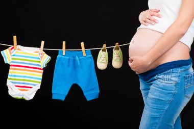 Çocuk giysileri siyah bir arka plan ile duran hamile kadın.