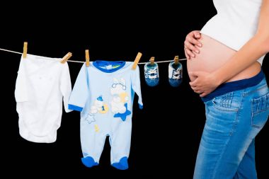 Çocuk giysileri siyah bir arka plan ile duran hamile kadın.