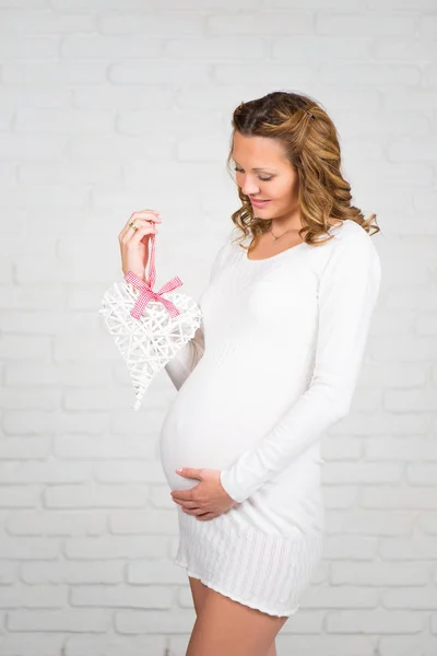 Gravid mamma innehar sitt hjärta över magen. Kärlek till sitt ofödda barn. — Stockfoto