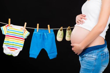 Çocuk giysileri siyah bir arka plan ile duran hamile kadın.