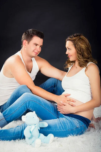 Embarazo pareja acostada abrazándose sobre un fondo negro —  Fotos de Stock