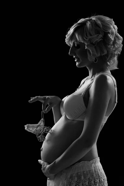 Zwanger meisje met een speelgoed koets op haar buik op een zwarte achtergrond. — Stockfoto