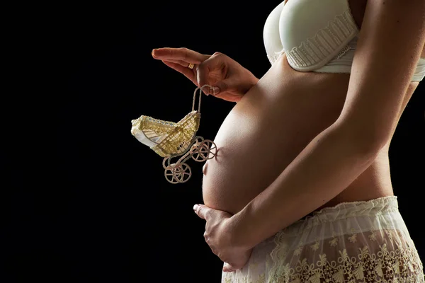 검은 배경에 그녀의 배에 장난감 캐리지 임신한 여자. — 스톡 사진