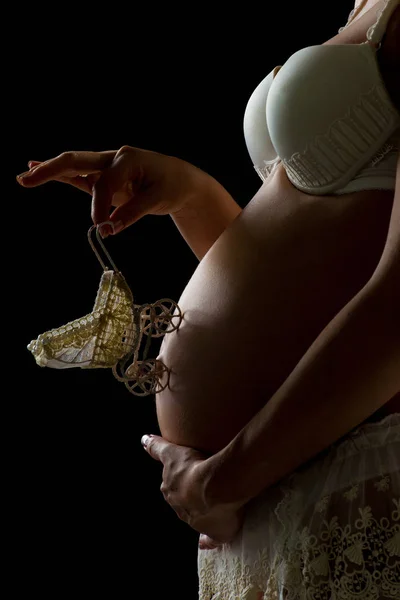 Zwanger meisje met een speelgoed koets op haar buik op een zwarte achtergrond. — Stockfoto