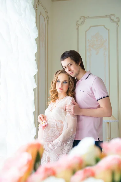 Schönes Paar, eine schwangere junge Frau und ein Mann, die sich liebevoll umarmen, im Inneren des Hauses — Stockfoto